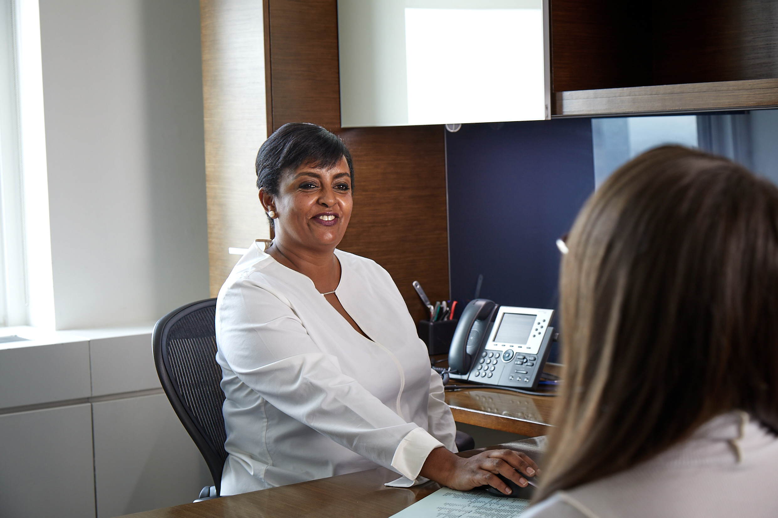 Lazard Woman Sitting at Desk Talking to Colleague Across from Her